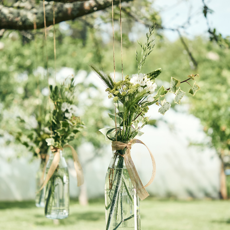 Sage green wedding decoration of foliage and flowers in a hanging clear glass bottle with rustic ribbon.