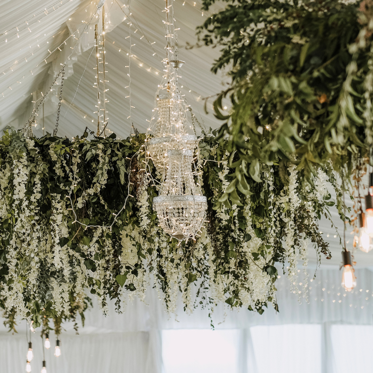 Sage green wedding marquee decoration of crystal chandelier and green leafy hanging foliage.