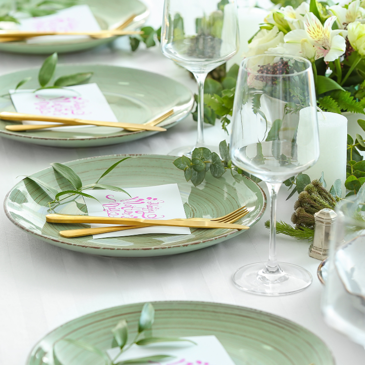 Sage green wedding table setting with green ceramic plates and gold cutlery.