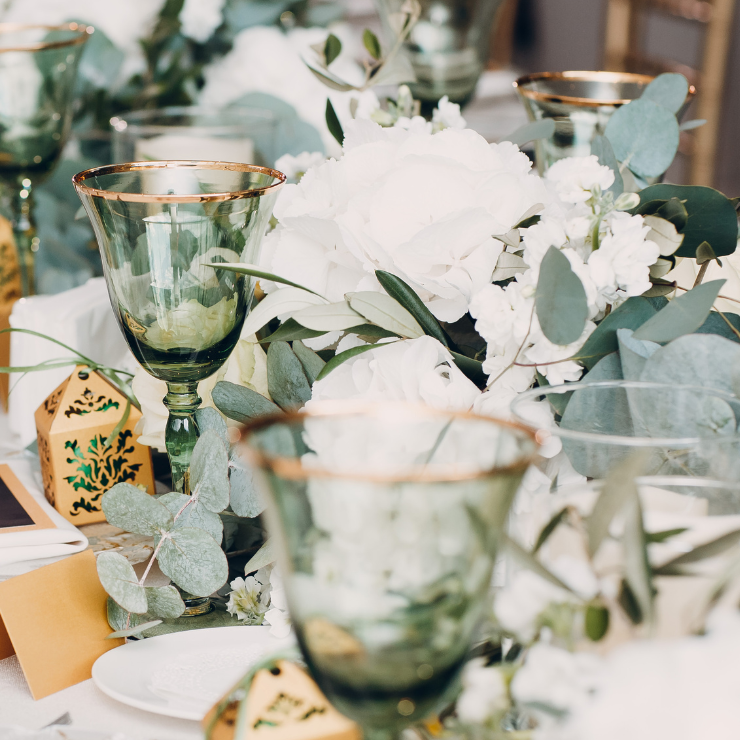 Sage green wedding table with green glass wine goblets, lantern and flower arrangements with eucalyptus leaves and white roses.