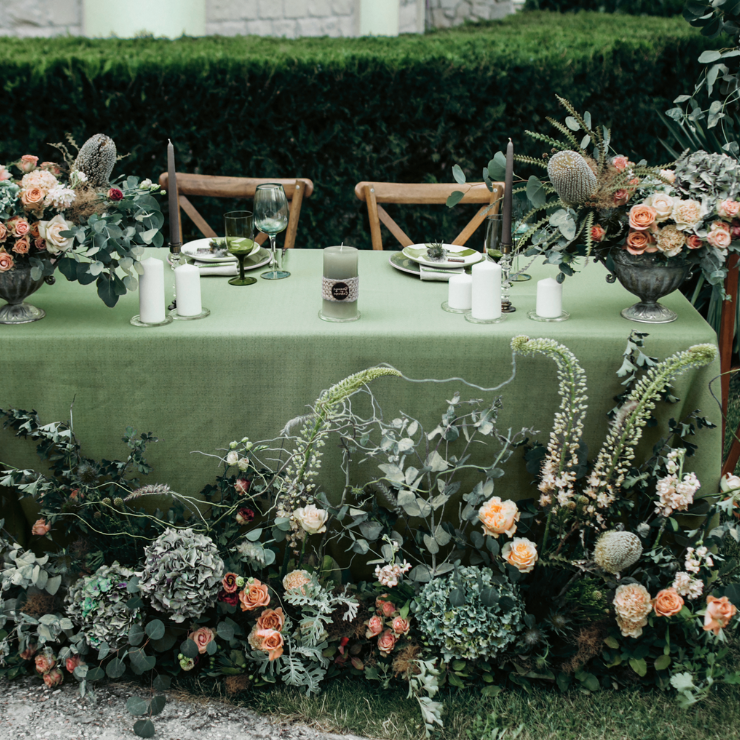 Sage green wedding table with green table cloth, candles and extravagant floral arrangements with sage green foliage and peach roses.