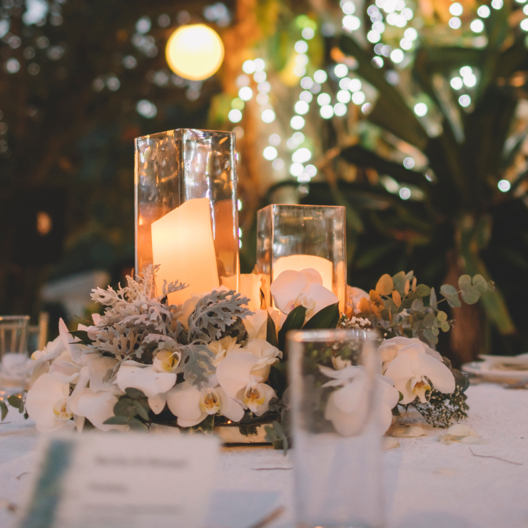 Sage green wedding decoration with candles in square glass vases, white orchids, eucalyptus leaves and sage green foliage.