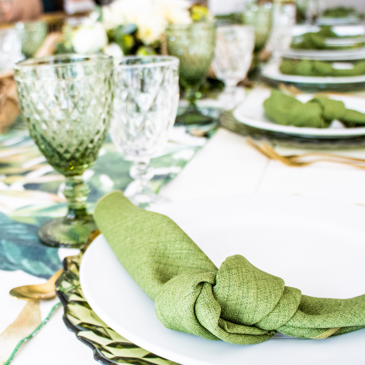 Sage green wedding table setting with ornate green dinnerware, glasses and sage green fabric napkins.