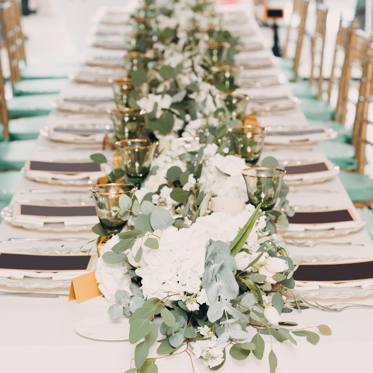 Sage green wedding reception table with green wine glasses and eucalyptus and white floral centerpiece decorations.