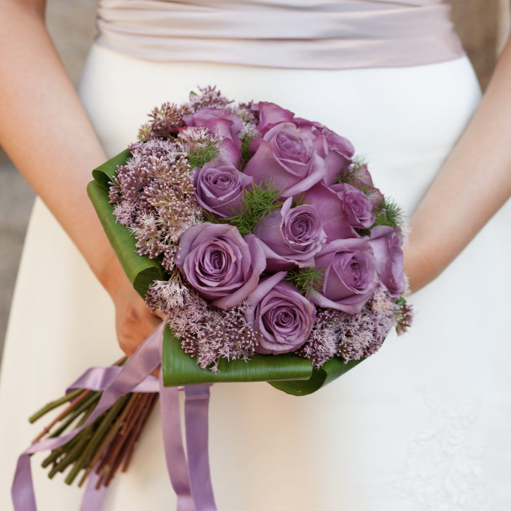 Dusty mauve bridal bouquet of dusty mauve roses and large green folded leaves, mauve silky ribbon being held by bride.