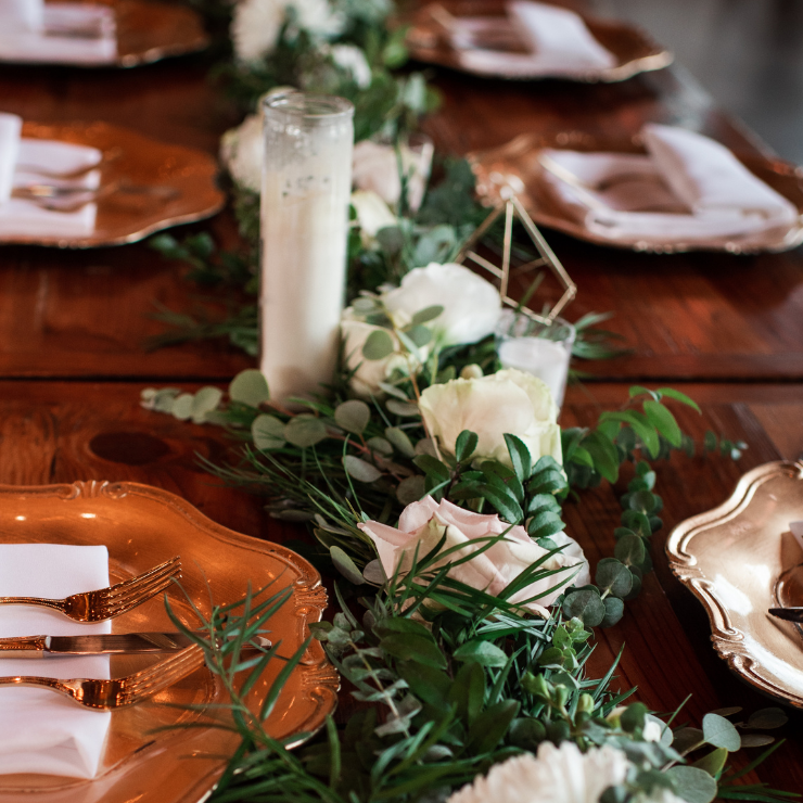 Sage green wedding rustic table setting with candle, vintage plates and green foliage and roses floral arrangement.