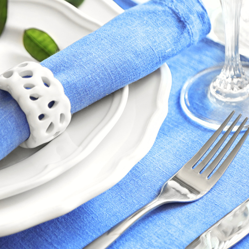 blue rolled up napkin with ring, white dinner setting on blue placemat