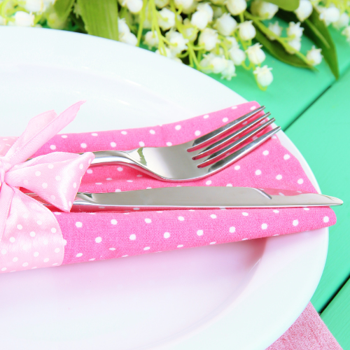 Coquette bridal shower theme inspiration image of cutlery with pink polka dot napkin and bow on a white plate with lily of the valley flowers.