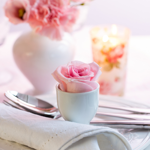 Coquette bridal shower theme inspiration image of table setting with pink peony, rose, white plate, cloth napkin and floral candle.