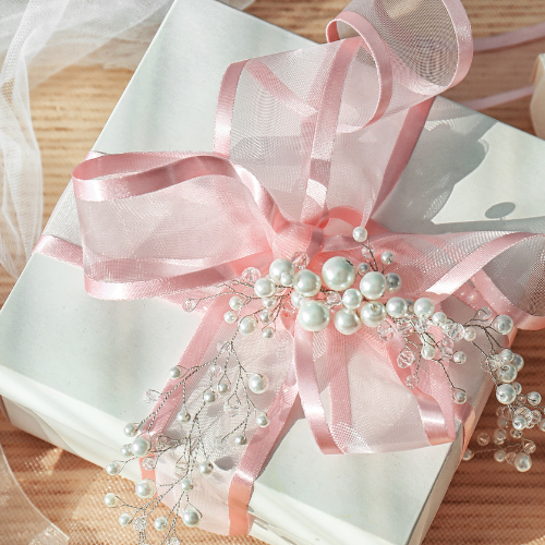 Coquette bridal shower theme inspiration image of bridal shower gift with blush pink organza and silk bow and pearls.